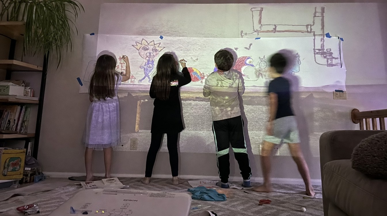 Four kids from behind at a paper wall, projected creatures walking